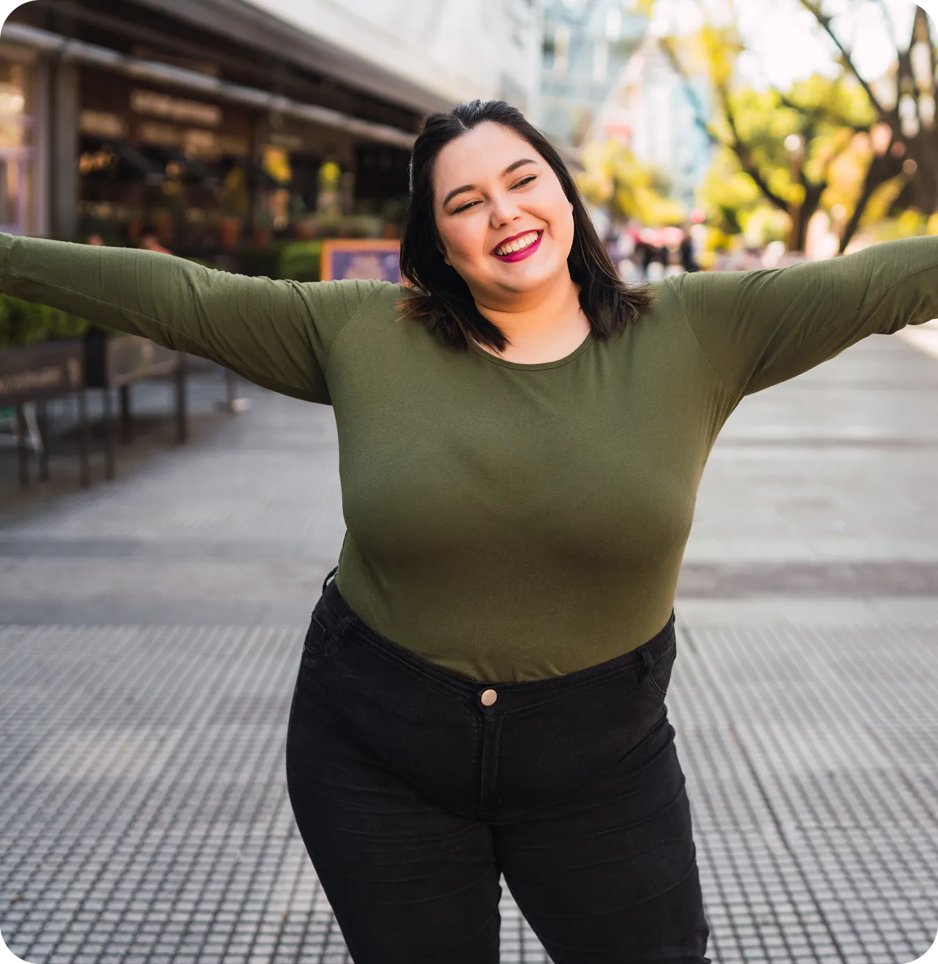 Smiling woman with her arms stretched out on a city street